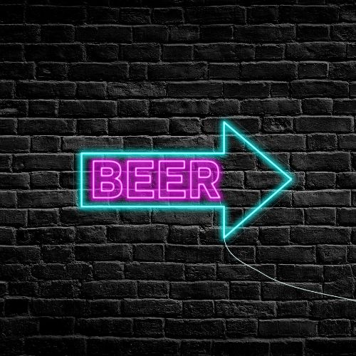 A neon beer sign inside an arrow pointing right is illuminating in a dark room with brick walls in the background