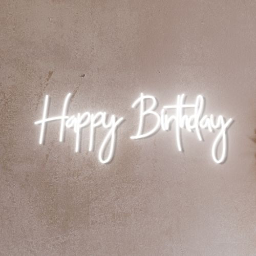 Bright neon Happy Birthday sign illuminating a dark room, with colorful letters spelling out the celebratory phrase